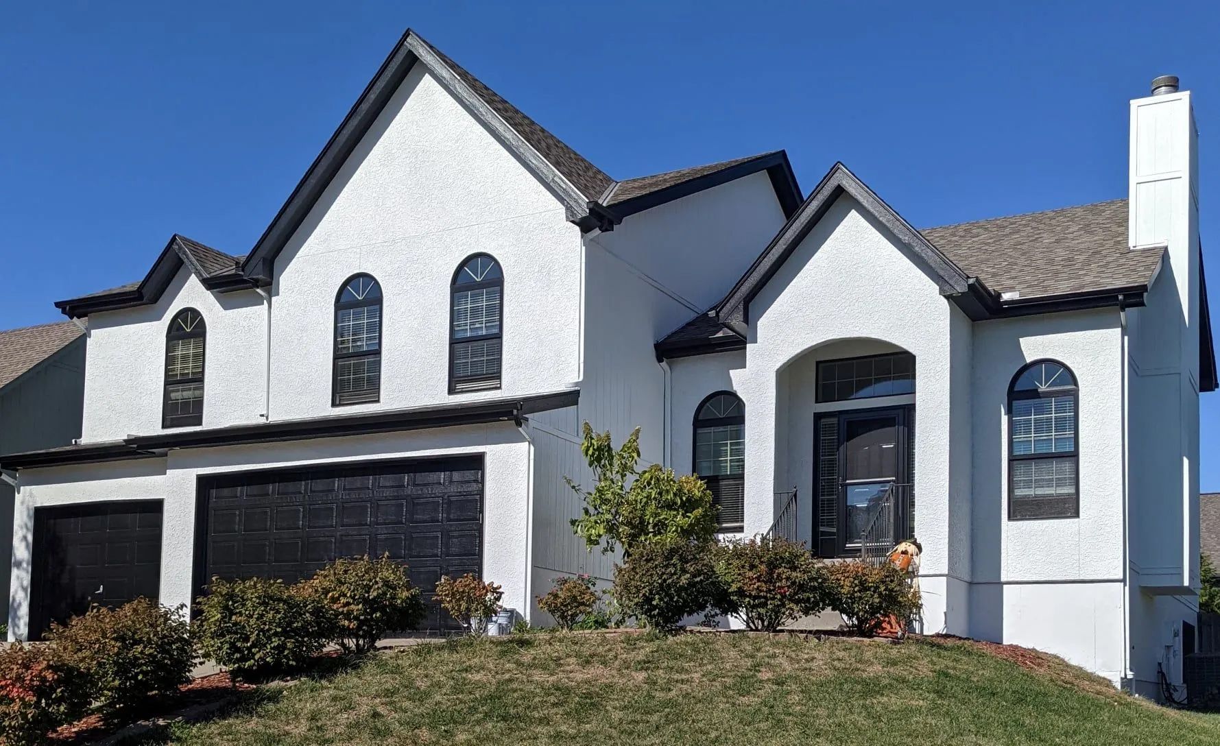 White stucco house with dark trim and doors, black garage doors, and a blue sky.
