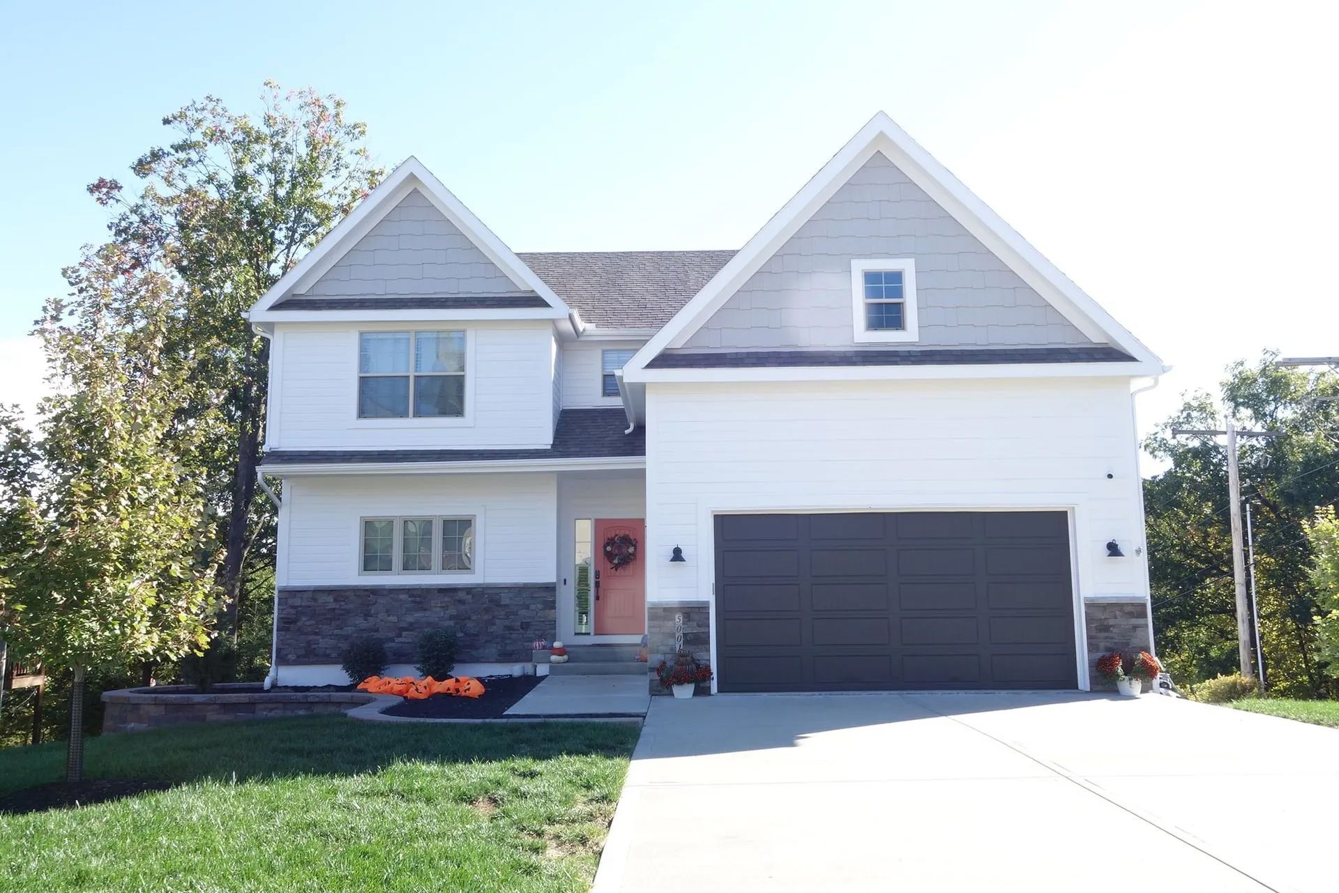 Two-story white house with gray accents and a dark gray garage door, on a sunny day.