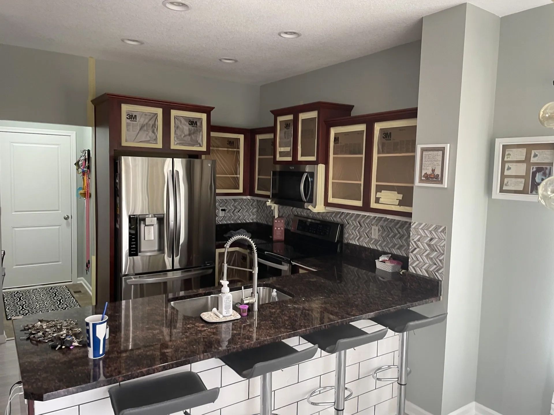 Kitchen with brown cabinets, dark countertops, stainless steel fridge, and a breakfast bar with stools.