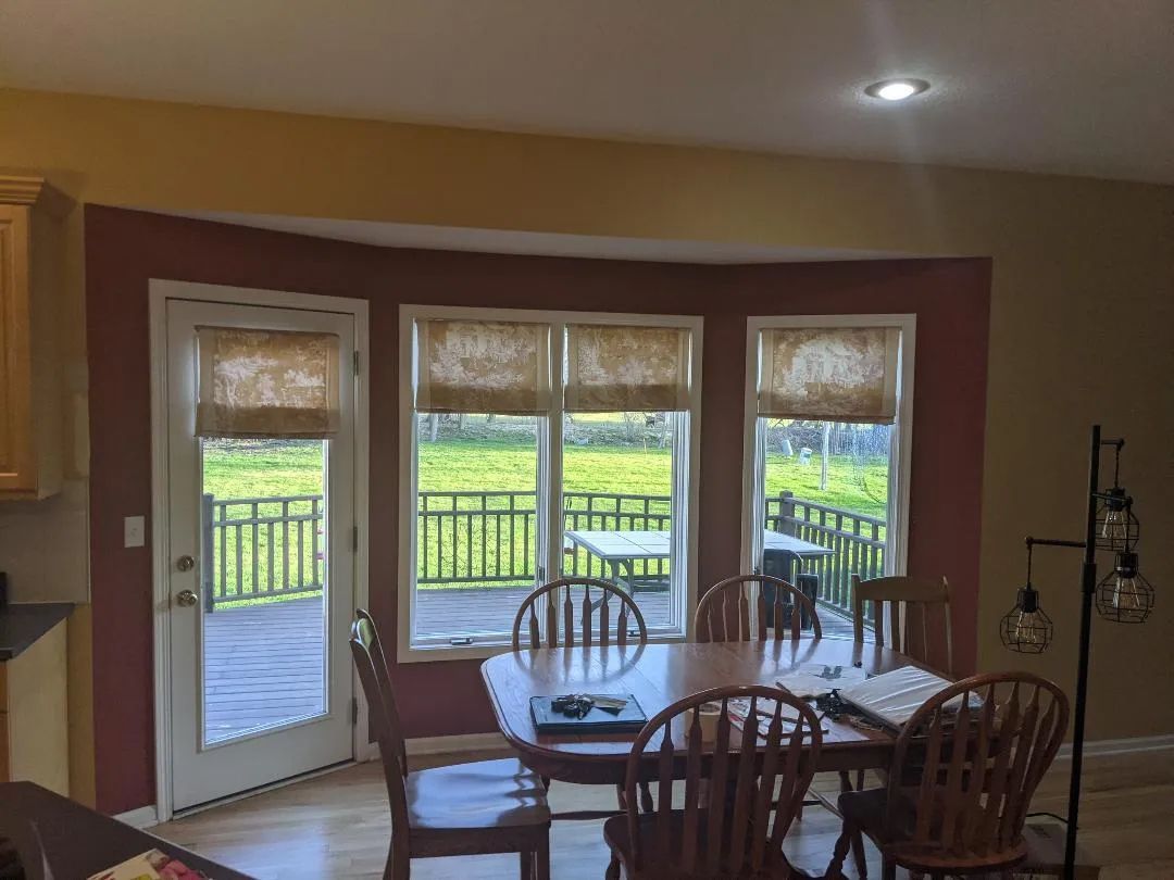 Dining room with wooden table and chairs, three windows with blinds, and a door leading to a deck.