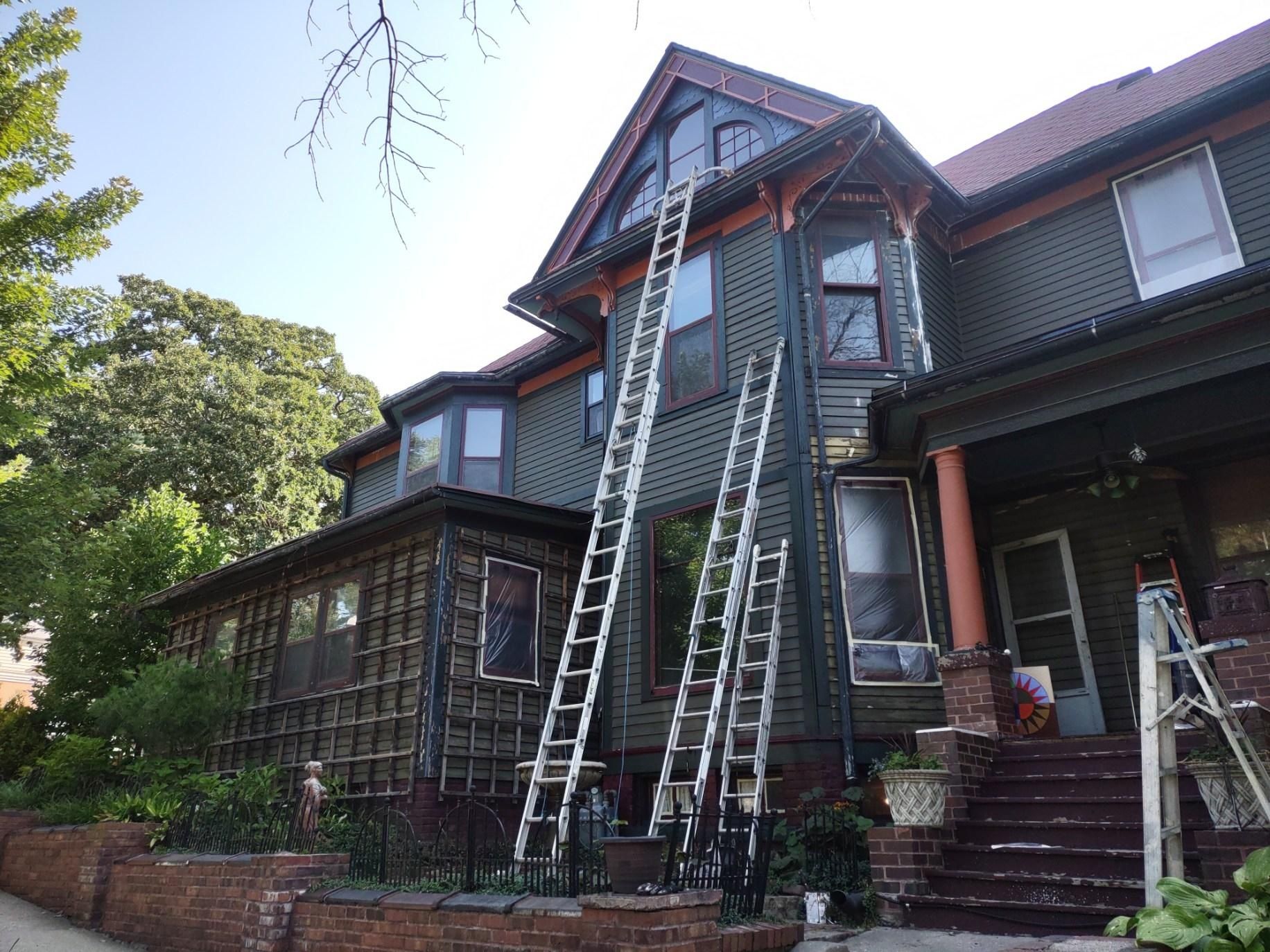 Three ladders propped against a Victorian house, exterior work in progress.