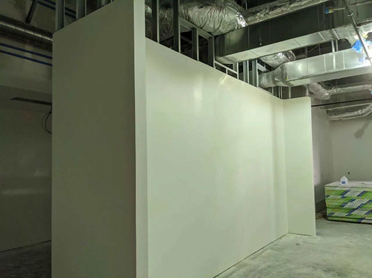 White walls of an interior room under construction, with exposed metal framework and ventilation ducts overhead.