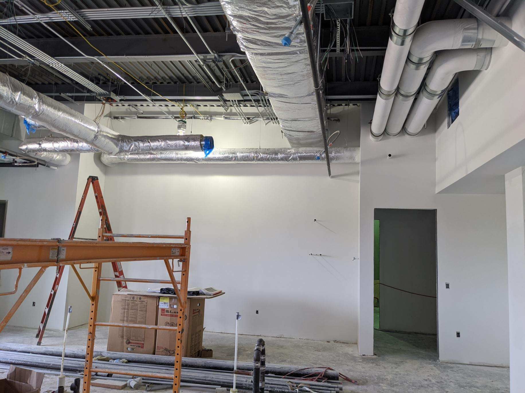 Construction interior: scaffolding, HVAC ducts, unfinished walls.