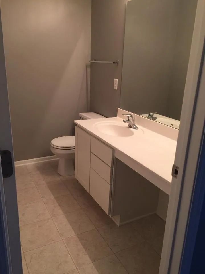 Bathroom with a white sink, toilet, and cabinets. Gray walls and beige tile floor.