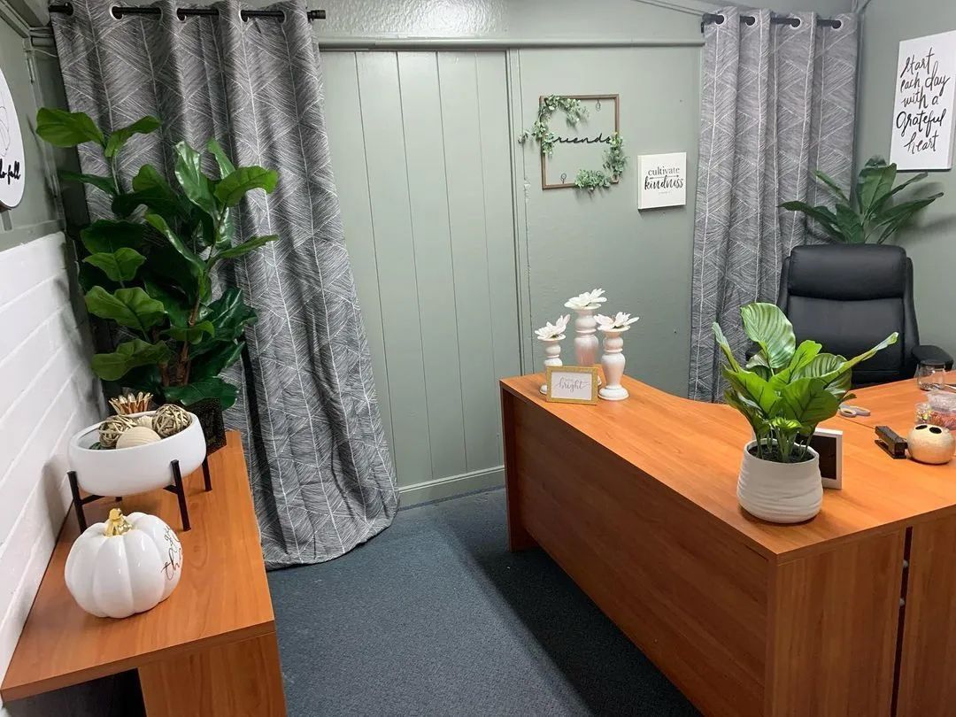 Office with desk, plants, curtains, and a sage green wall.