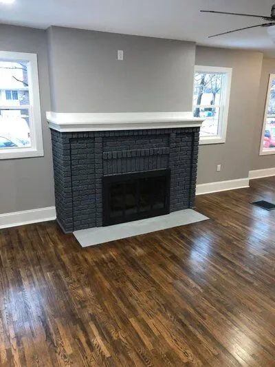Black brick fireplace with gray walls, white trim, and dark wood floors.