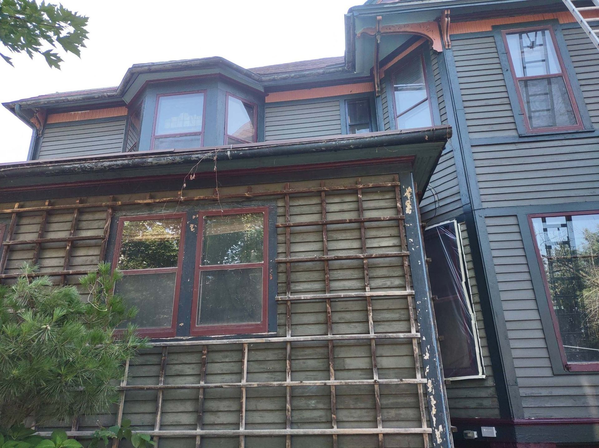 Weathered Victorian house with dark siding, bay windows, and deteriorating exterior.
