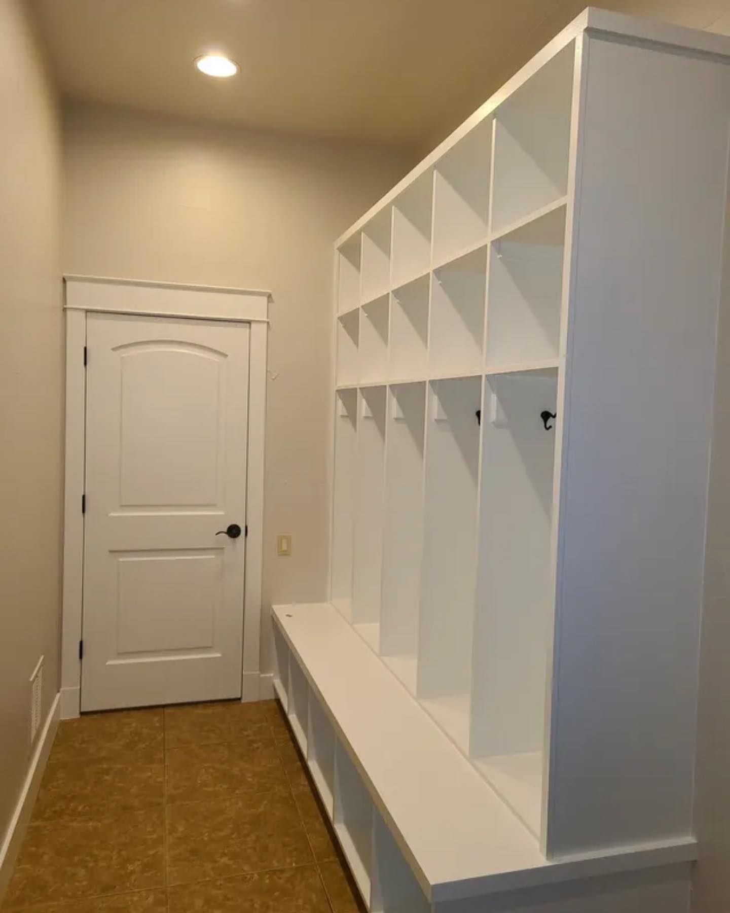 White locker storage unit with hooks and bench in a hallway with a closed white door.