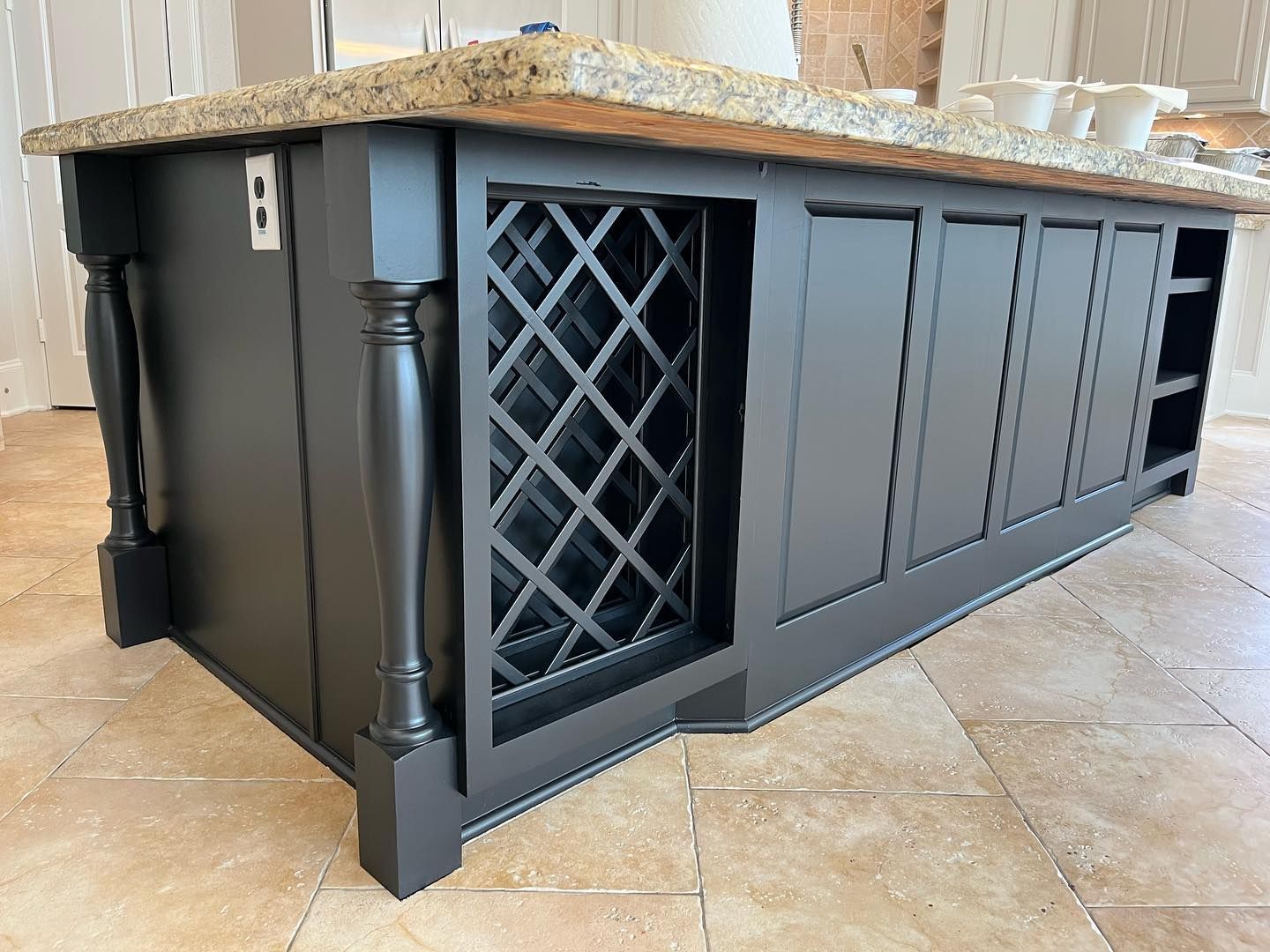 Black kitchen island with wine rack and cabinets, topped with granite countertop.