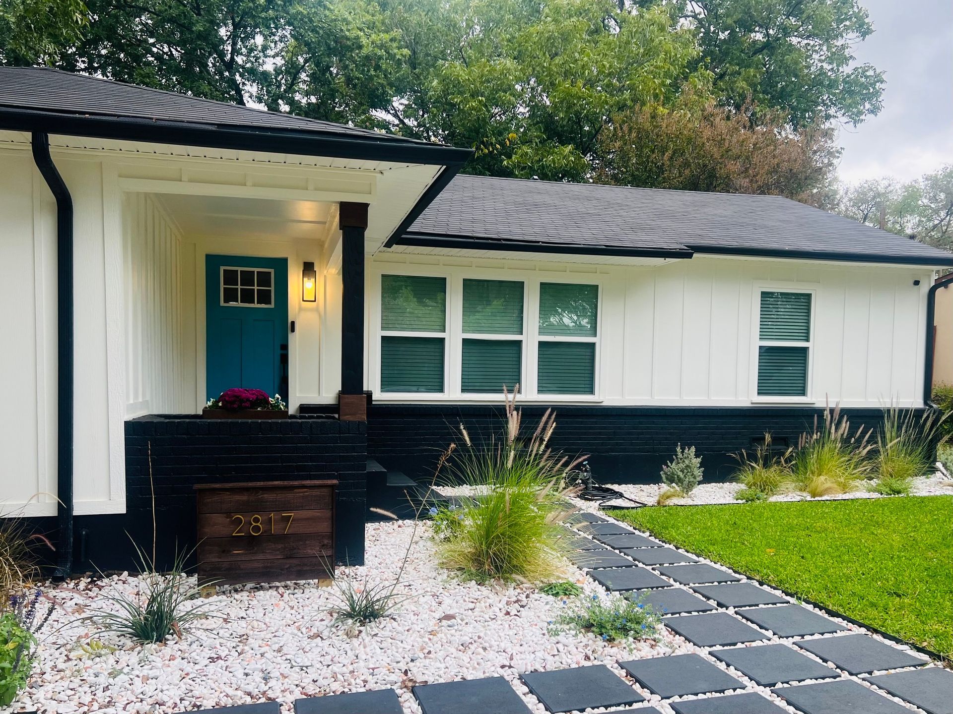 Blue house with white trim and front porch, American flag, under cloudy sky.