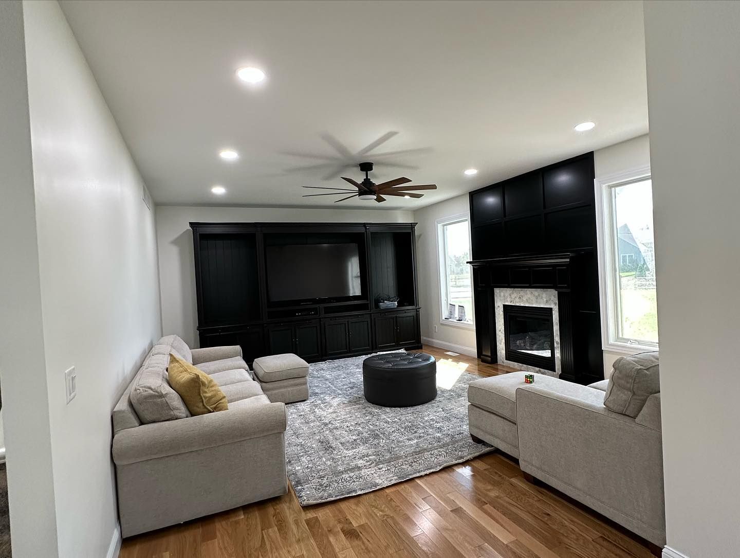 Living room with black entertainment center, fireplace, tan couches, and gray rug.