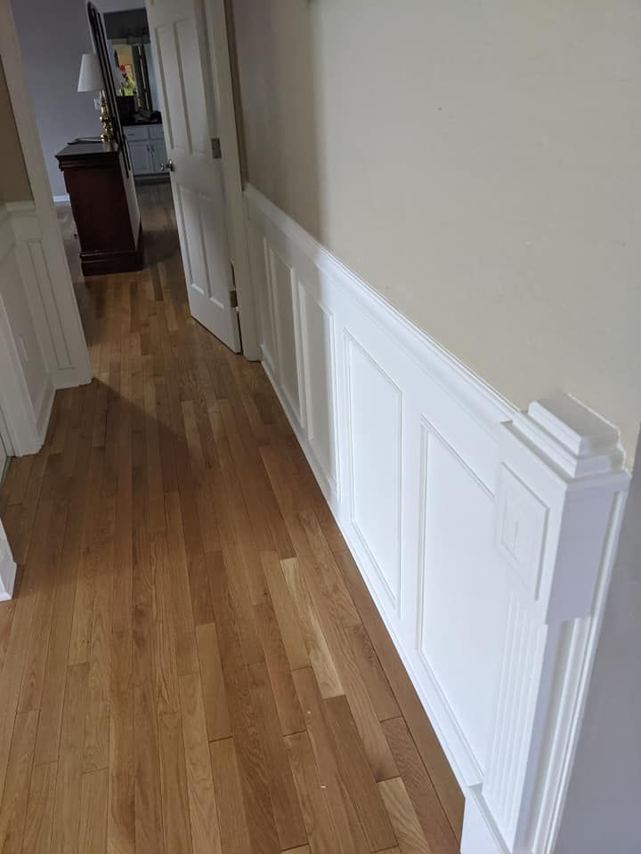 Hallway with white wainscoting, light wood floors, and a partially open white door.
