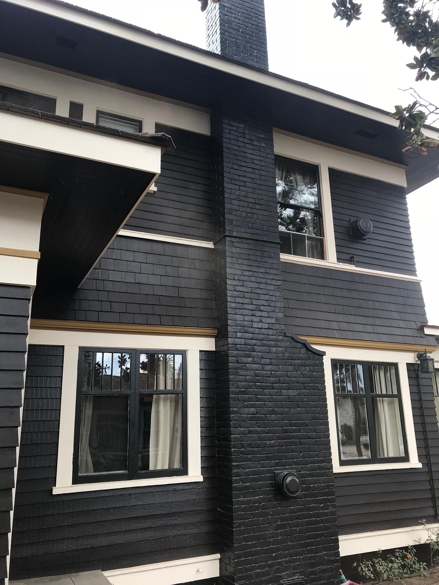 Black house with a brick chimney and white trim.