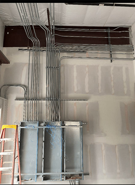 A ladder is sitting next to a wall with electrical wires hanging from it.