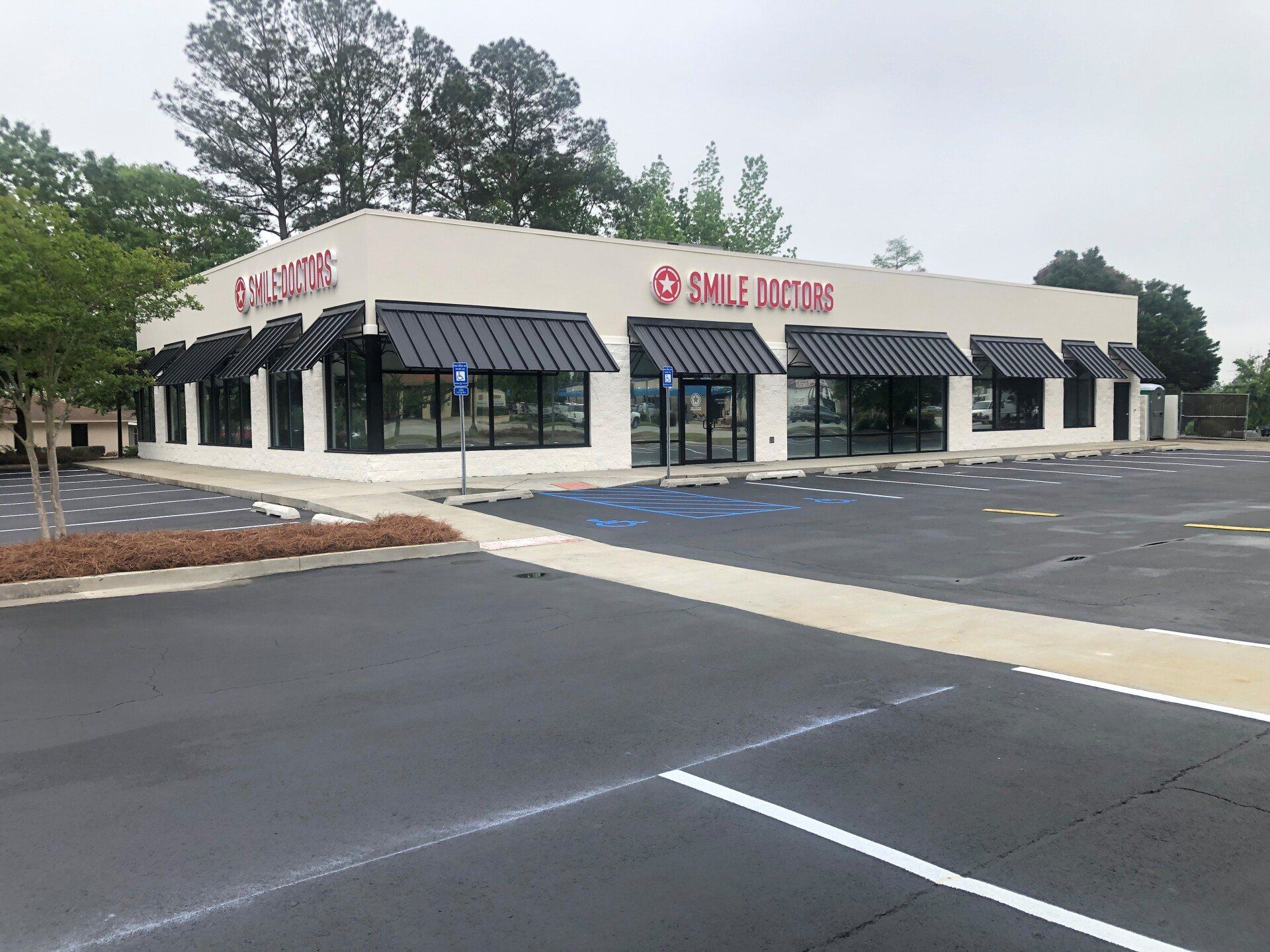 A large white building with black awnings and a parking lot in front of it.