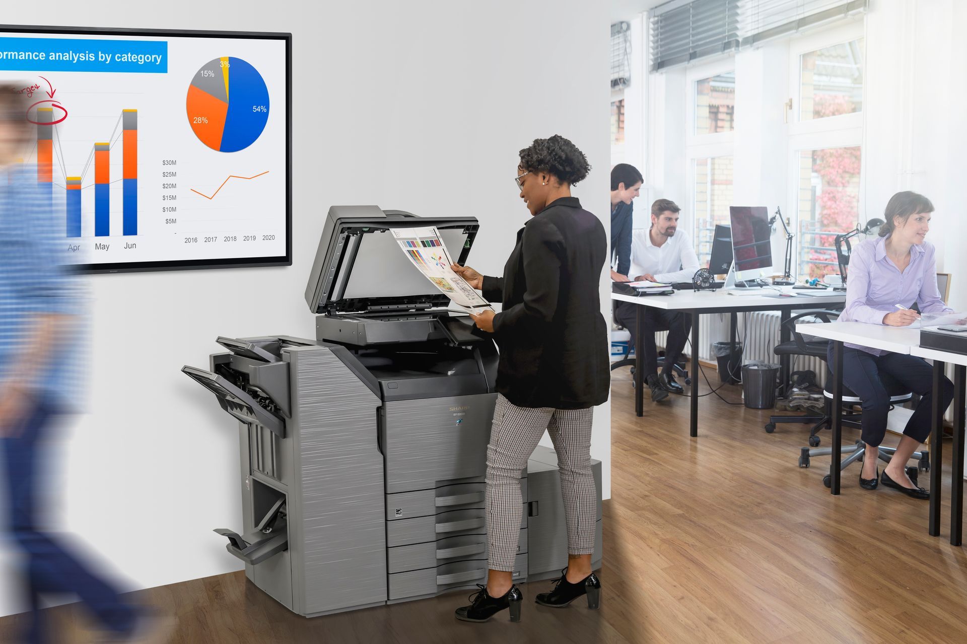 A woman is standing in front of a printer in an office.