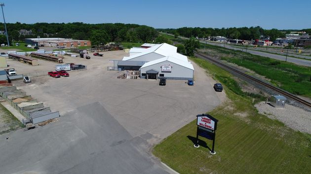 Aerial view of a white event tent on a large gravel lot beside railroad tracks and a roadside sign.