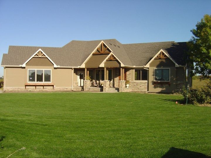 Single-story beige house with a front porch and large green lawn under a clear blue sky