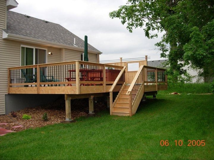 Wooden backyard deck with stairs beside a house, set on a green lawn.
