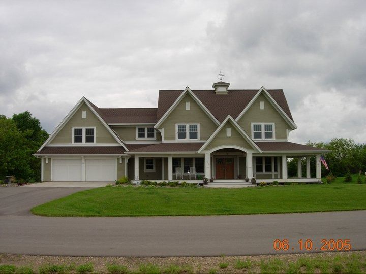Large green two-story house with a front porch and attached garage on a cloudy day