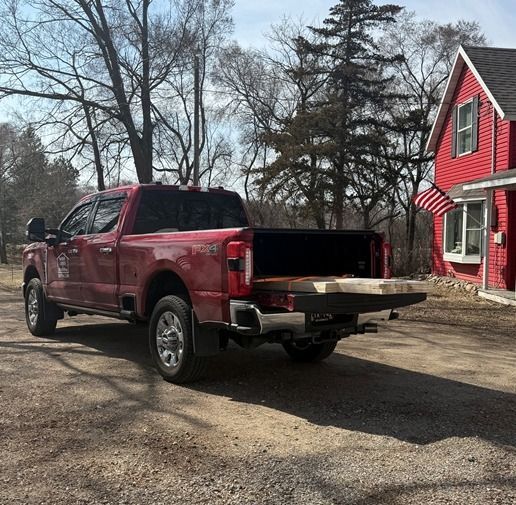 Red pickup truck with open tailgate parked in a driveway beside a red house