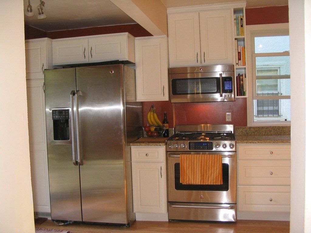 Compact kitchen with stainless steel refrigerator, stove, microwave, and white cabinets