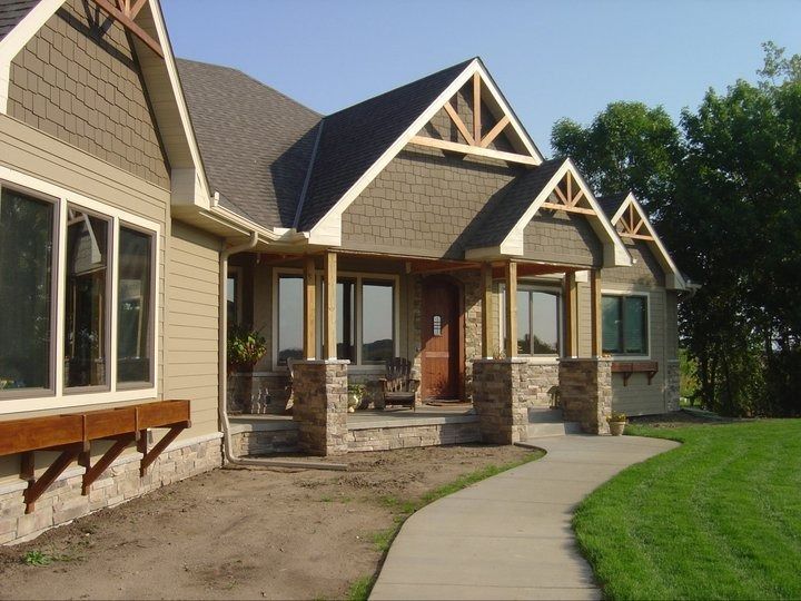 Modern suburban house with stone columns, curved walkway, and green lawn on a sunny day