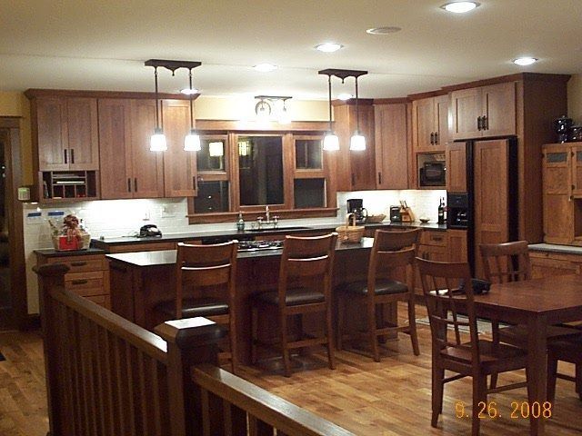 Warm wooden kitchen with island, bar stools, pendant lights, and hardwood floors at night.