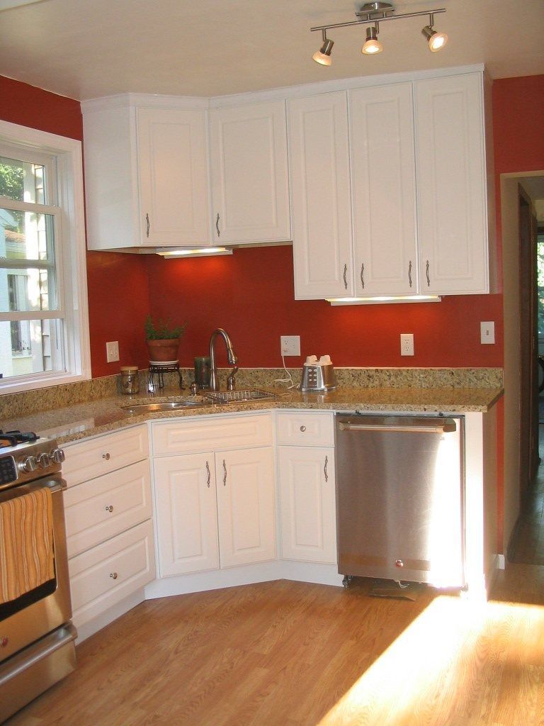 Kitchen with white cabinets, red walls, granite counters, and a stainless steel dishwasher under bright sunlight