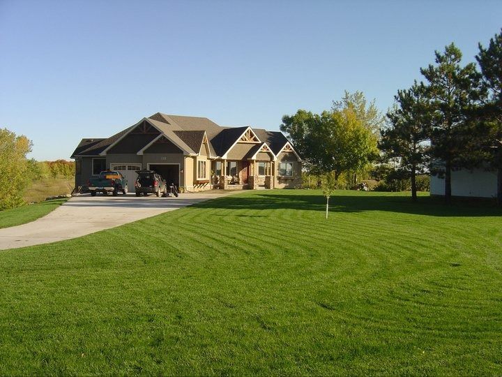 Suburban house with a large green lawn, driveway, and trees under a clear blue sky