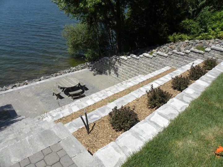 Steep stone steps and a picnic table leading down to a lakeside shoreline with plants and shade trees.