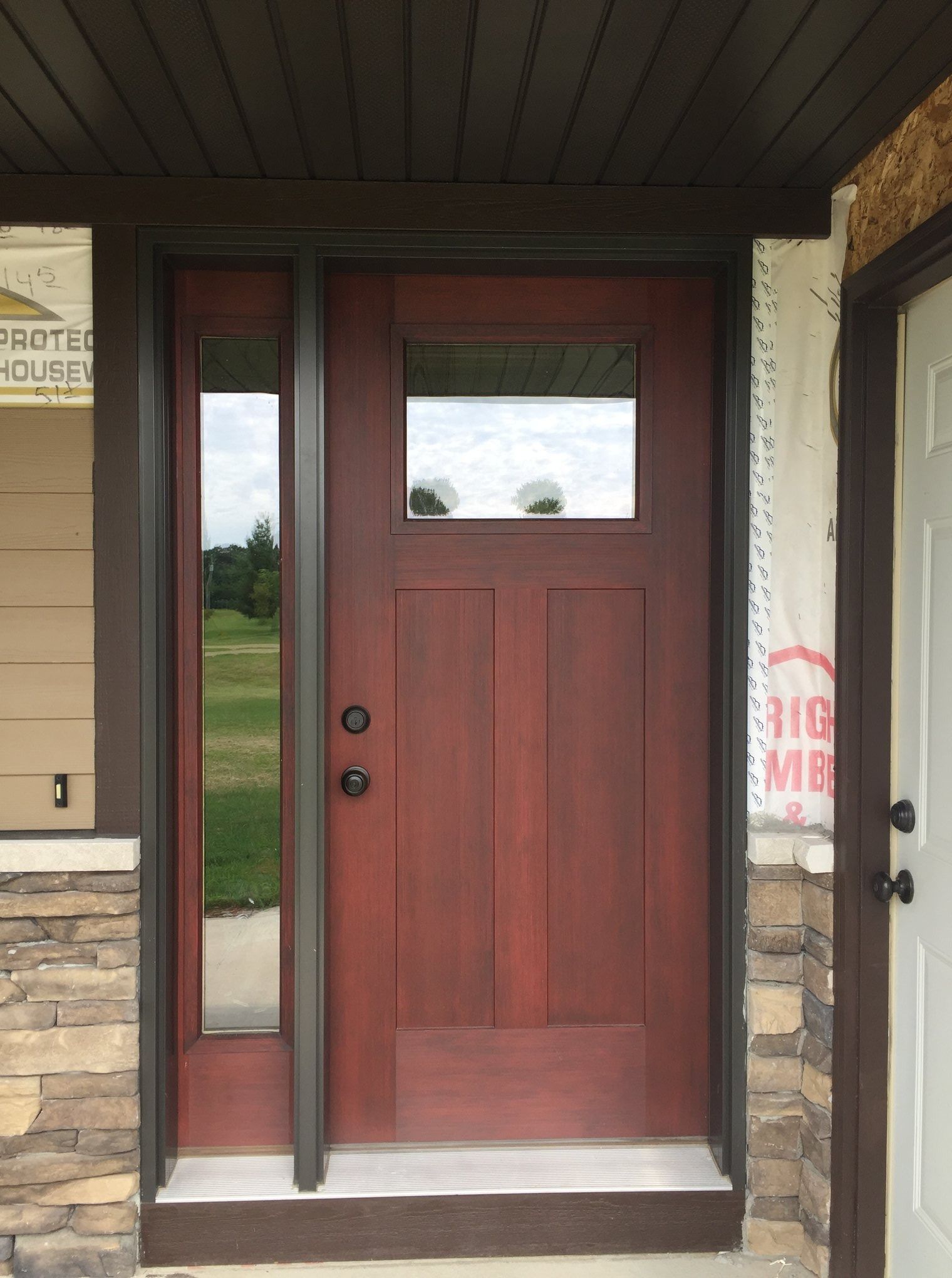 Red front door with narrow sidelights and a small upper window at a covered entryway