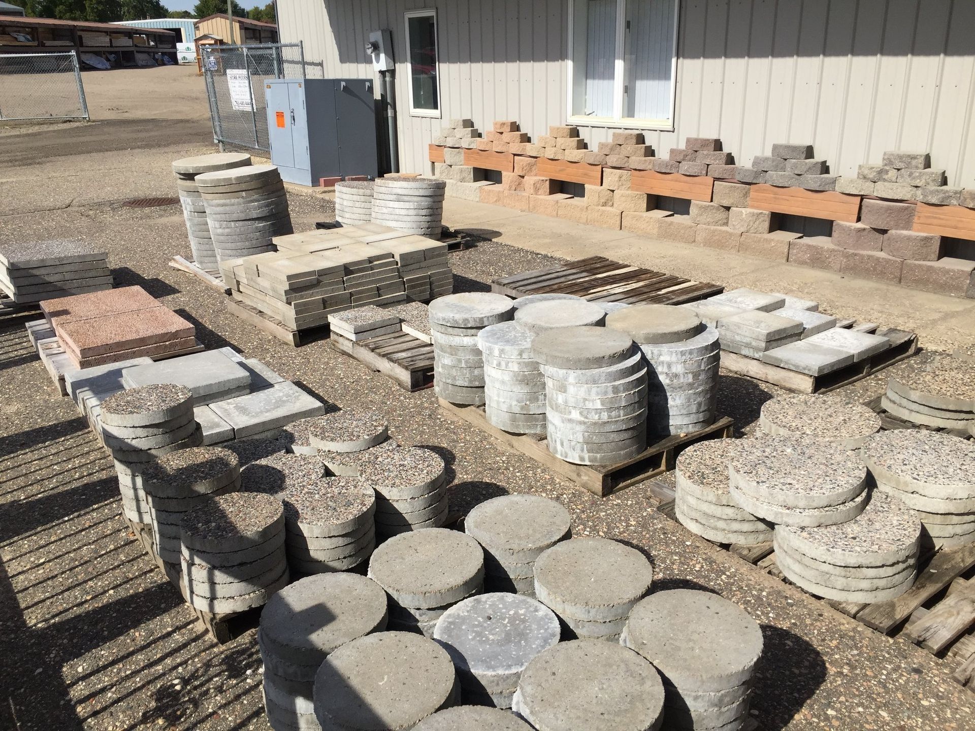 Stacks of stone pavers and concrete blocks arranged outdoors beside a building.