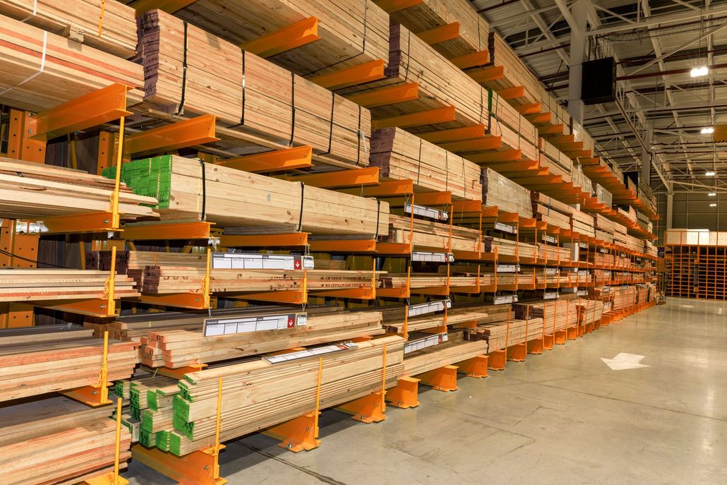 Warehouse aisle with rows of orange steel shelving stocked with lumber and a polished concrete floor