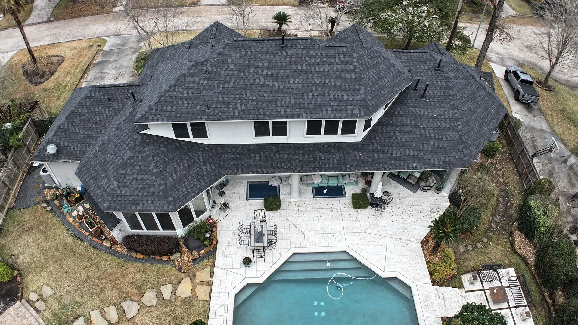 Aerial view of a gray-roofed house with a backyard pool and patio.