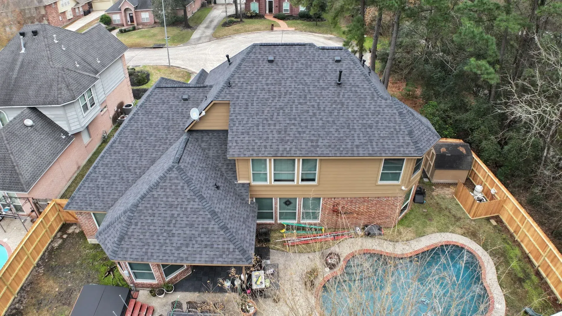 Aerial view of a two-story house with a dark roof, fenced yard, and swimming pool