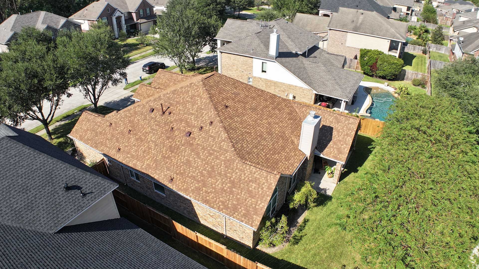 Aerial view of a suburban neighborhood with a tan-roofed house surrounded by trees and neighboring homes.