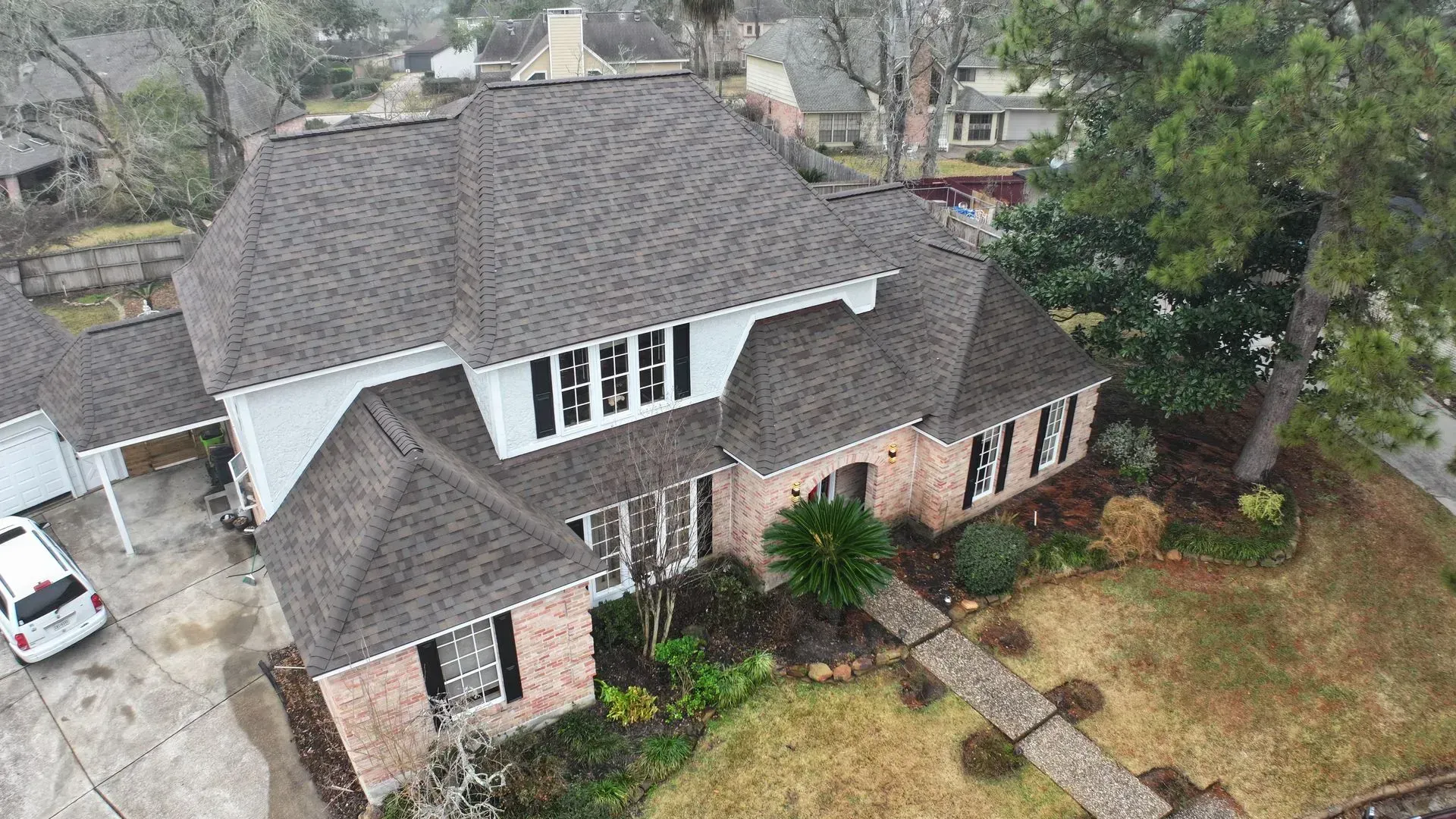 Aerial view of a brick house with a dark shingled roof and front yard trees