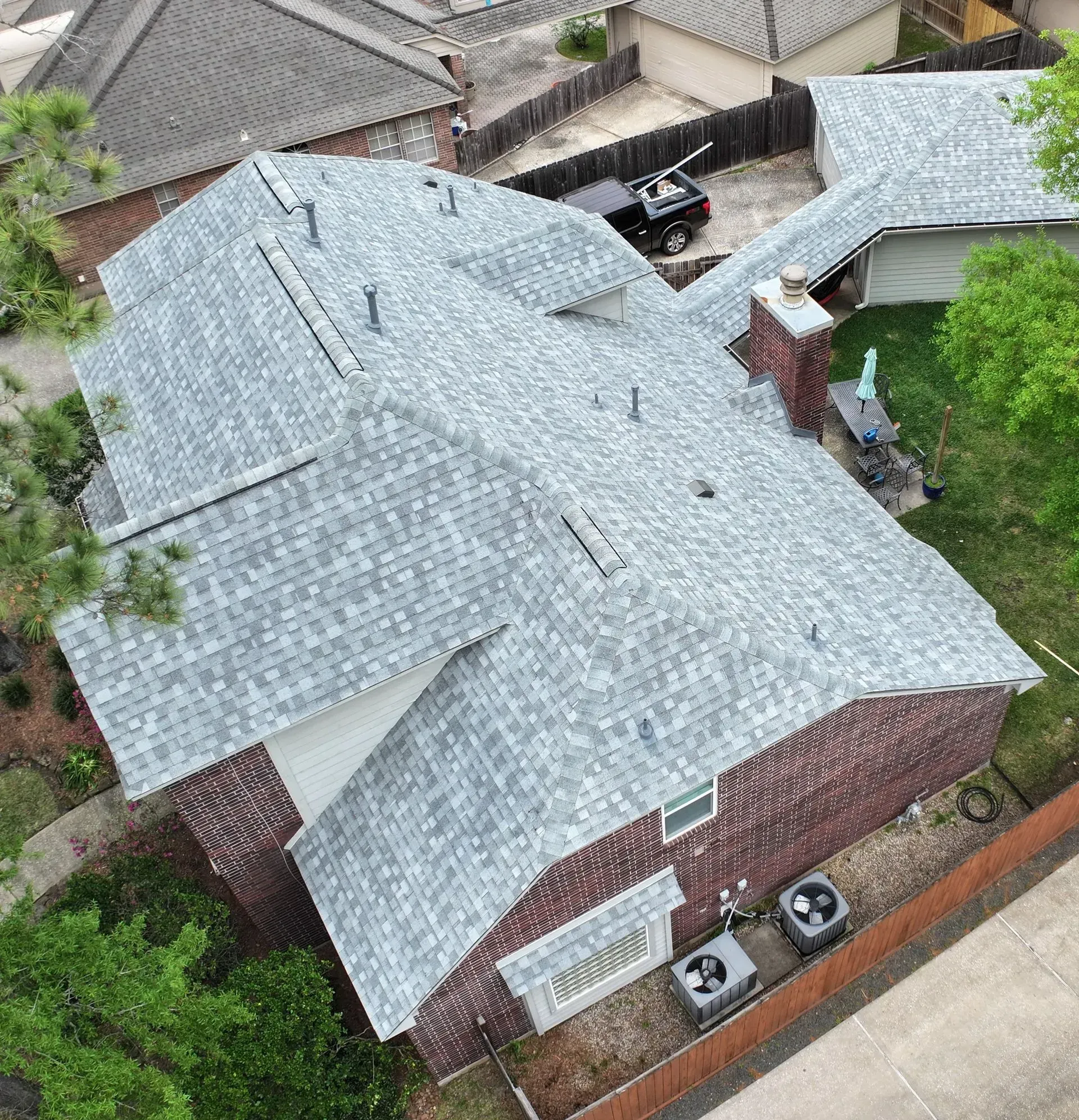 Aerial view of a brick house with a gray shingled roof in a residential neighborhood