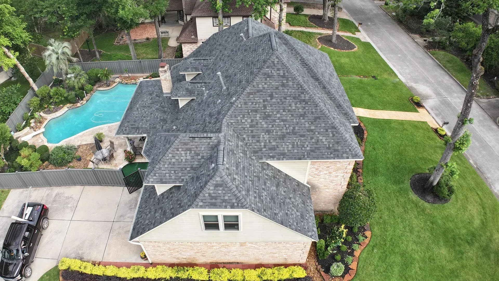 Aerial view of a suburban house with a gray roof, backyard pool, and landscaped lawn.