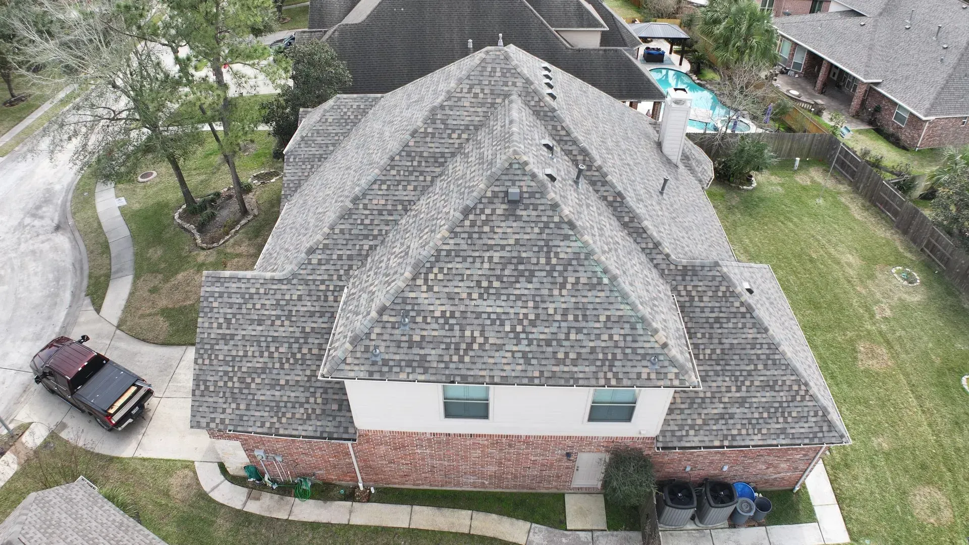 Aerial view of a gray-shingled house with a brick lower level and surrounding yard.