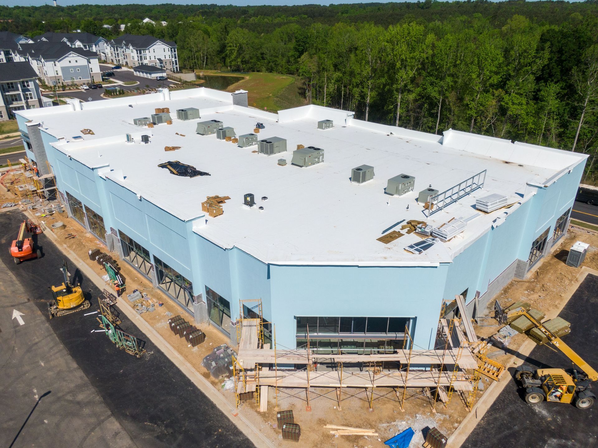 Aerial view of a large white industrial building under construction beside a forest