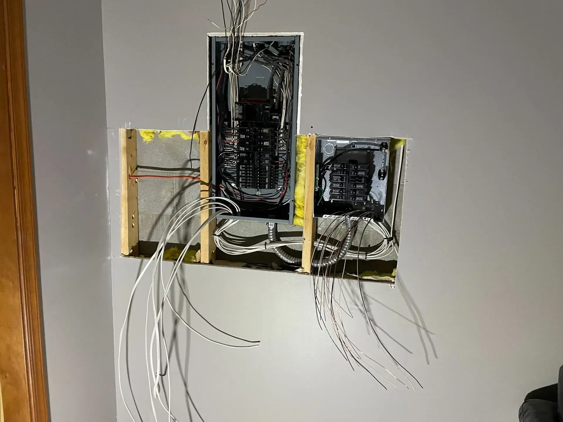 Two electrical panels mounted on a wooden frame against a gray wall, with several wires hanging from the units.