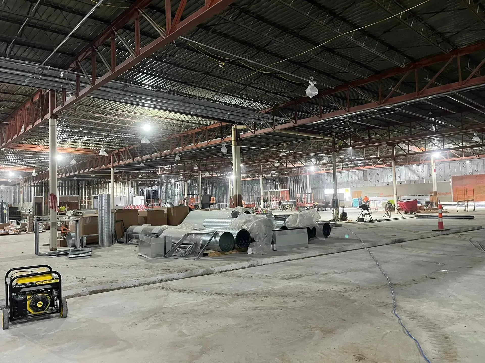 A large, industrial warehouse interior under renovation with exposed steel beams, construction equipment, and tools.