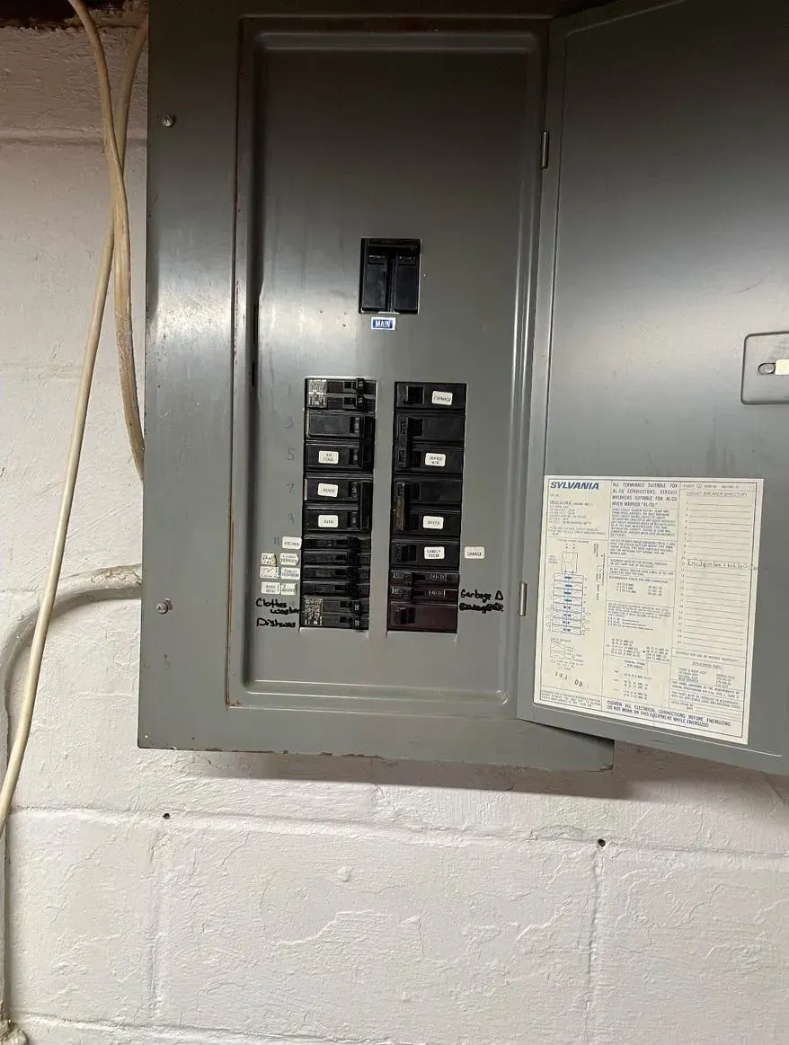 A gray electrical circuit breaker panel with switches, mounted on a white cinder block wall.