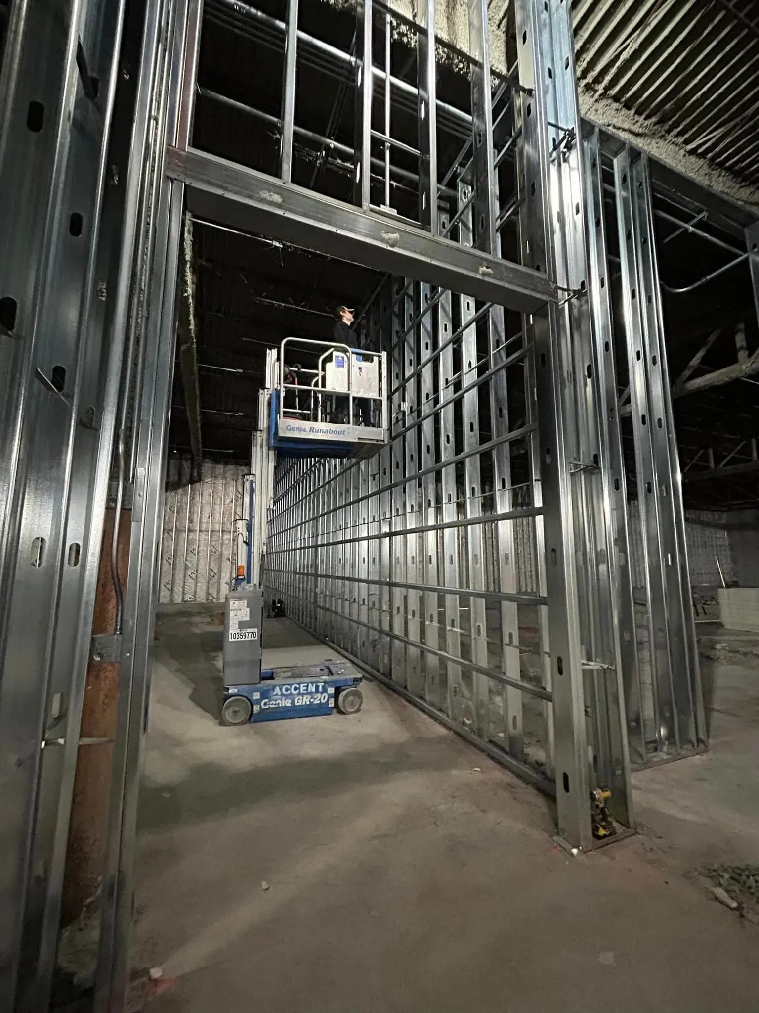 A blue industrial lift parked inside a building under construction with metal framing for walls and ceilings.