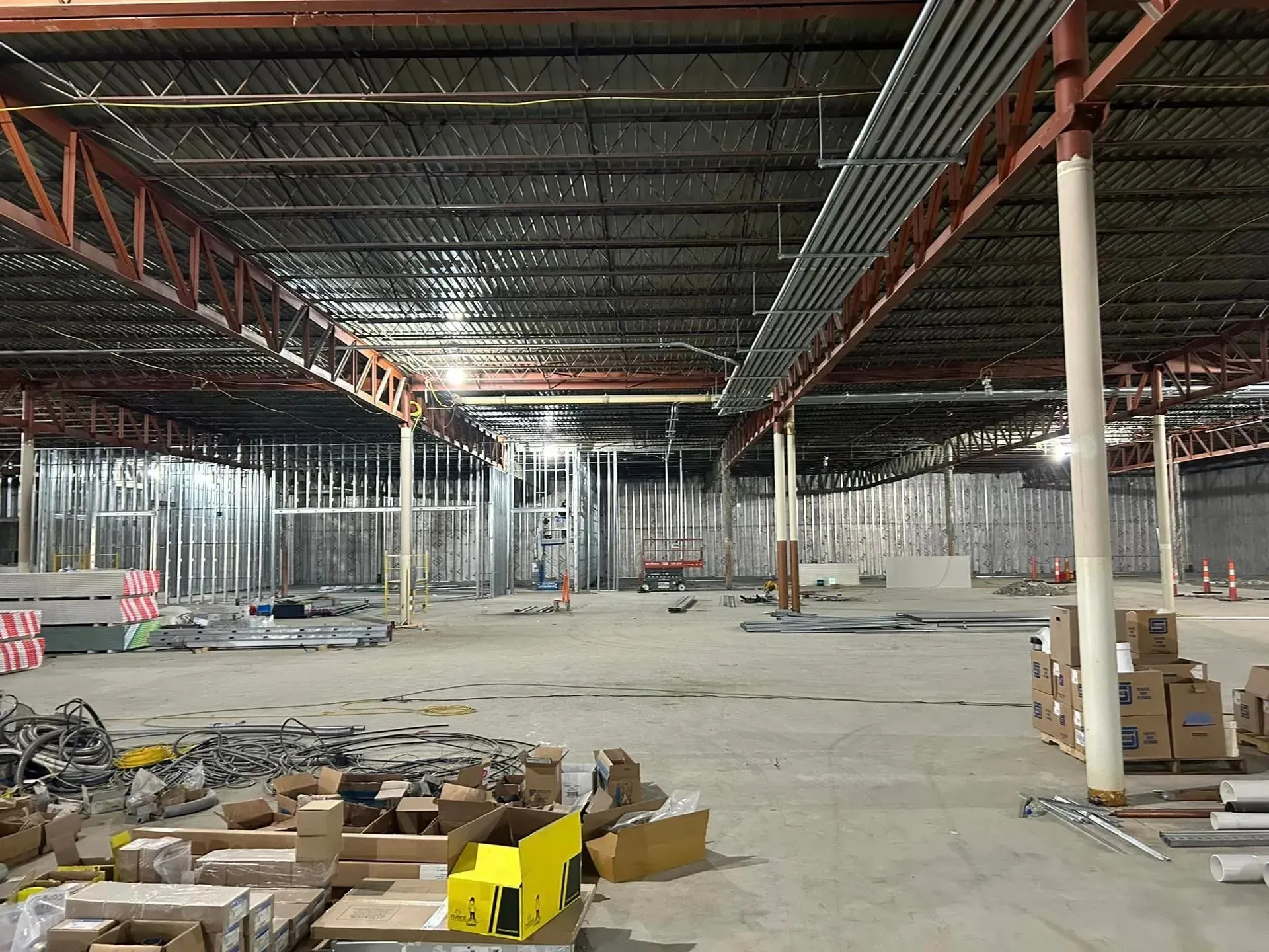 Construction site inside a large, open industrial space with metal framing, exposed ceiling beams, and scattered supplies.