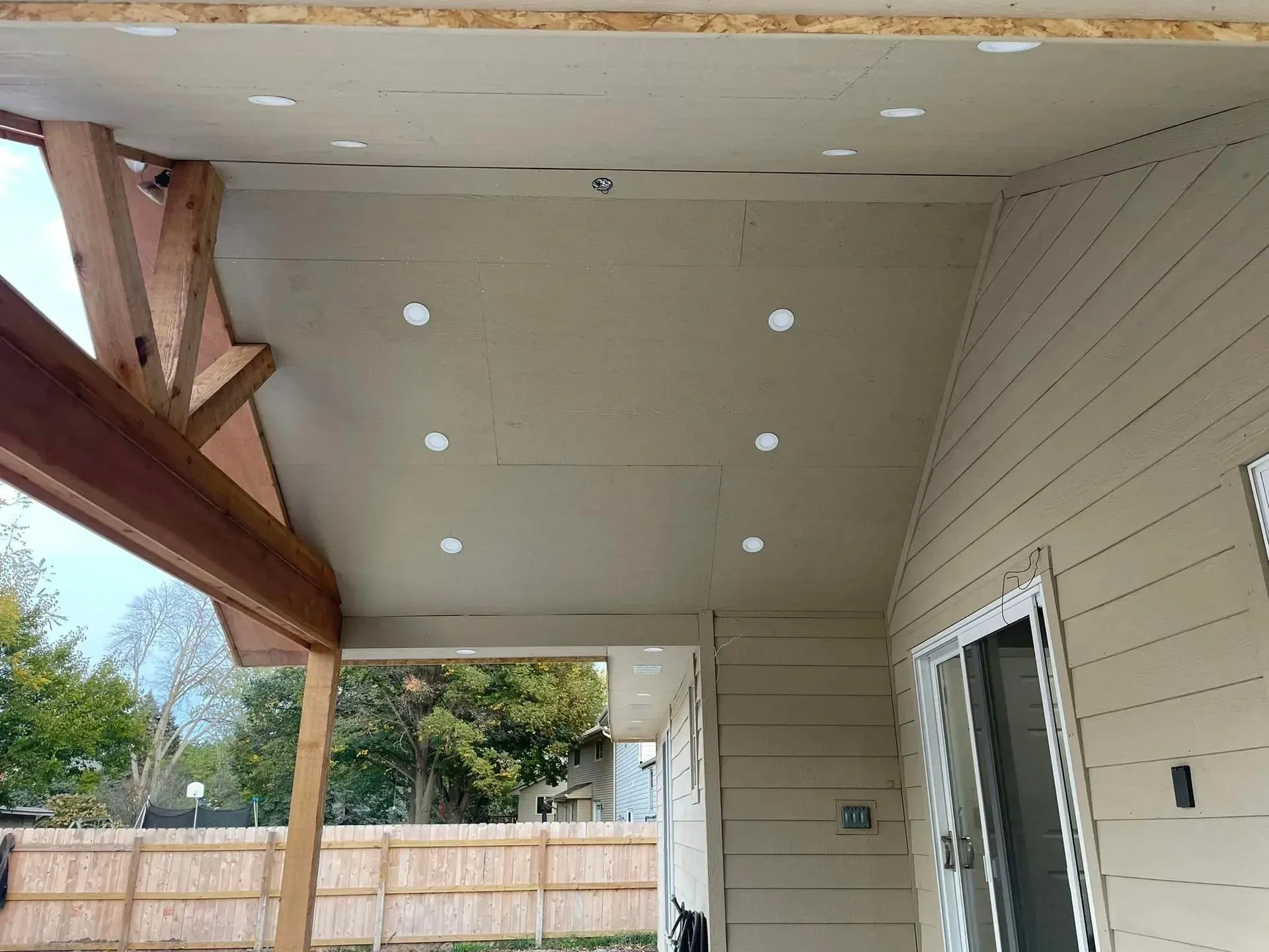 A wooden covered patio under construction featuring a beige ceiling with recessed lighting and a sliding glass door.