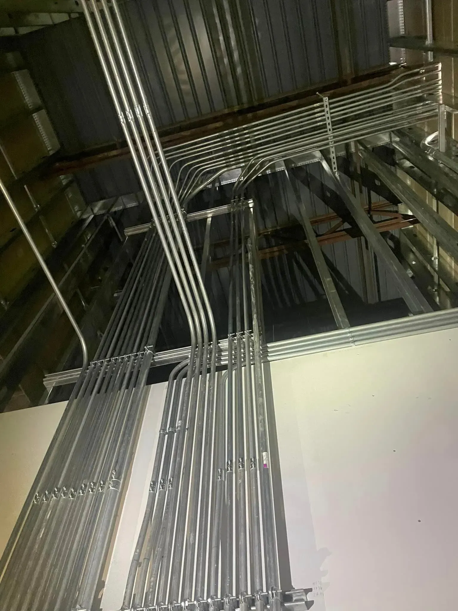 Numerous parallel metal electrical conduits run along a wall and ceiling, supported by metal brackets.