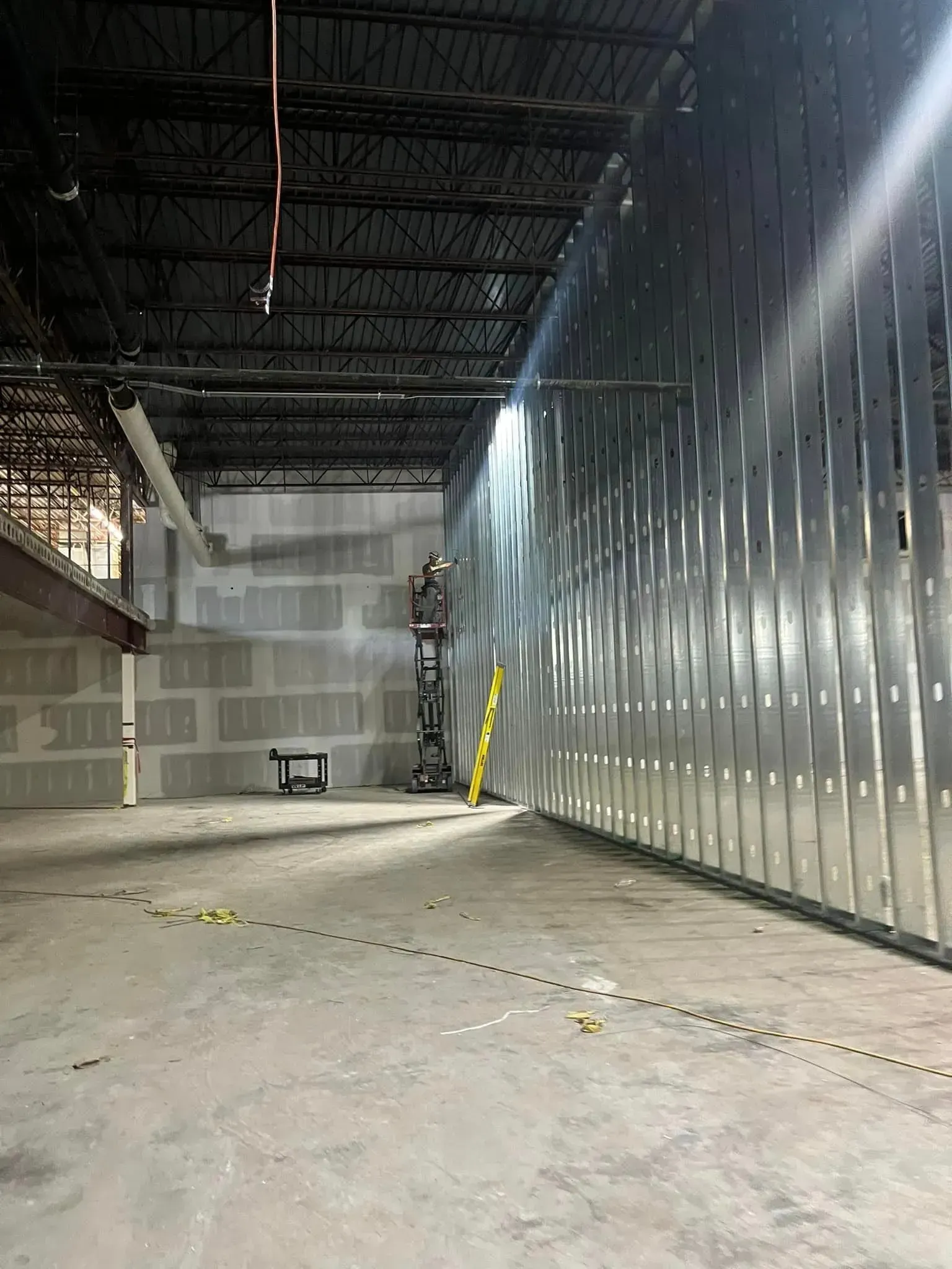 An unfinished commercial interior space with a tall metal stud wall on the right and a drywall partition in the back.